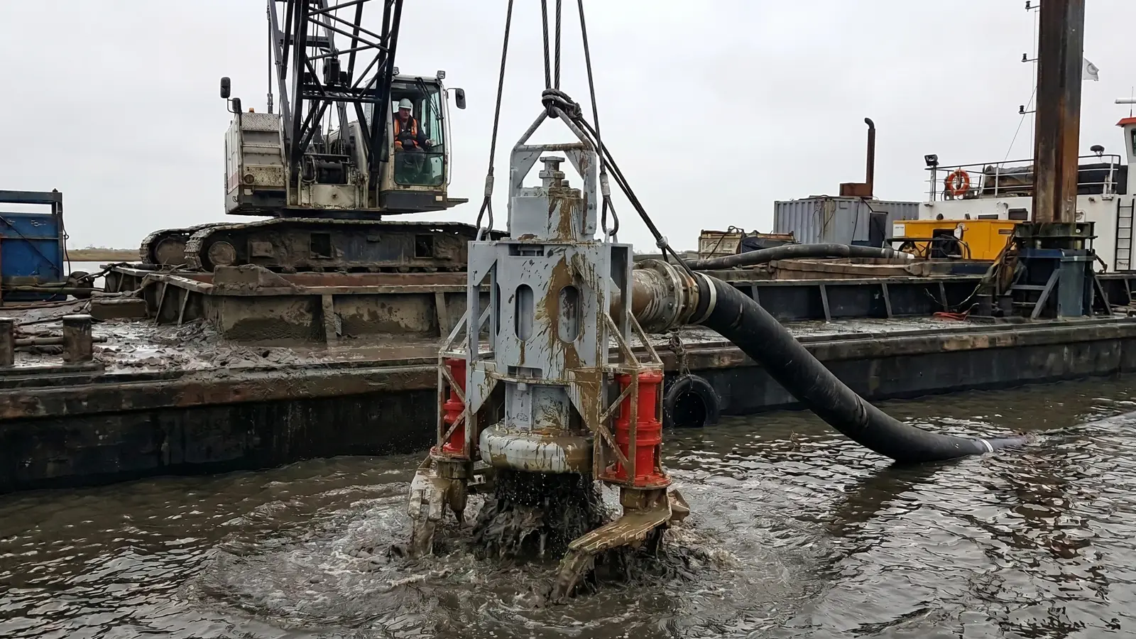 New, Used and Rental Dredge Pumps Crane lifting a DAE Pumps cable-deployed dredge pump out of the water beside a work barge